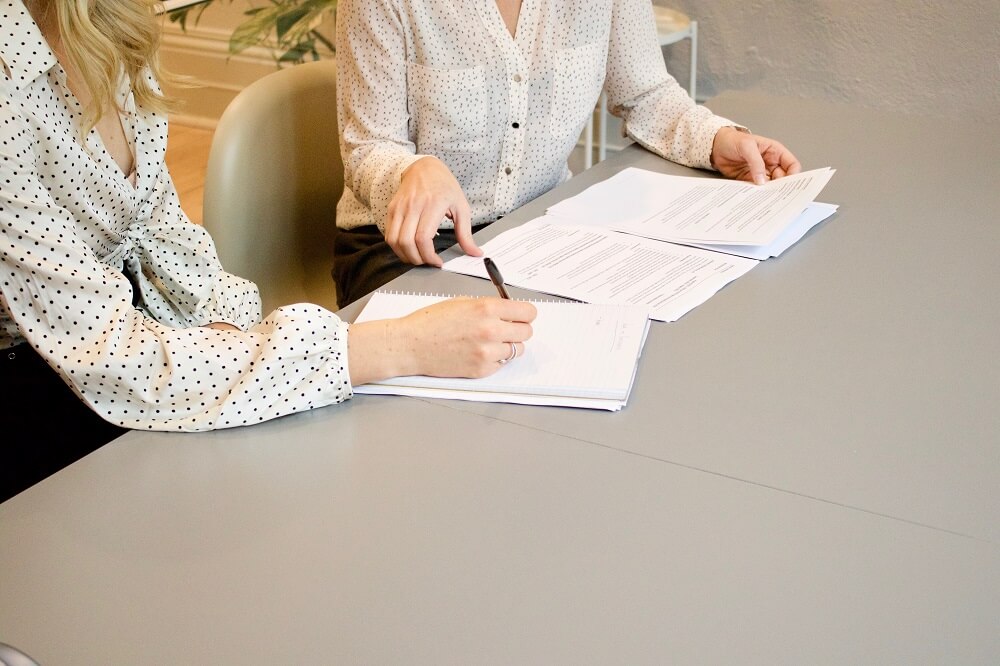 two businesswomen sat at a desk preparing confirmation statement documents